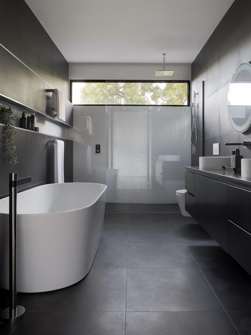 A dark-tiled bathroom with a freestanding tub and a long floating vanity.
