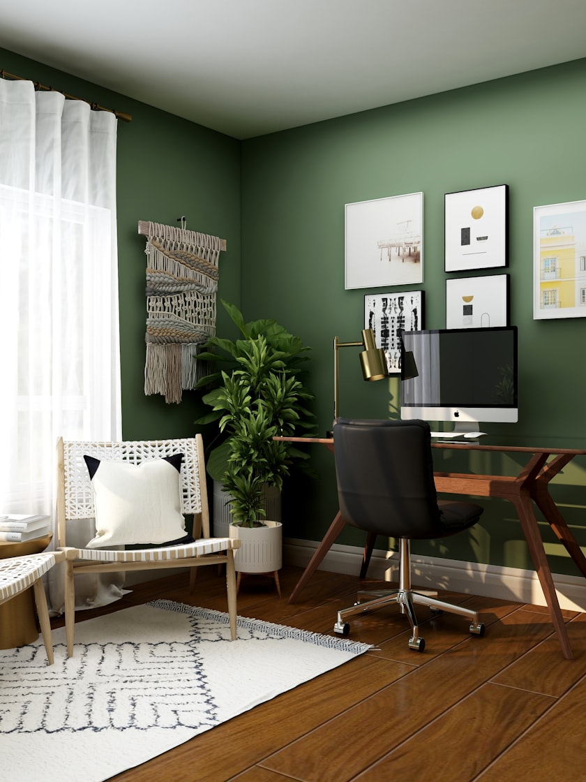 A study with a deep green wall, a timber desk and a framed picture wall.