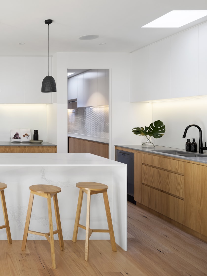 A kitchen with a pale stone island, timber cabinetry and a rooflight above.