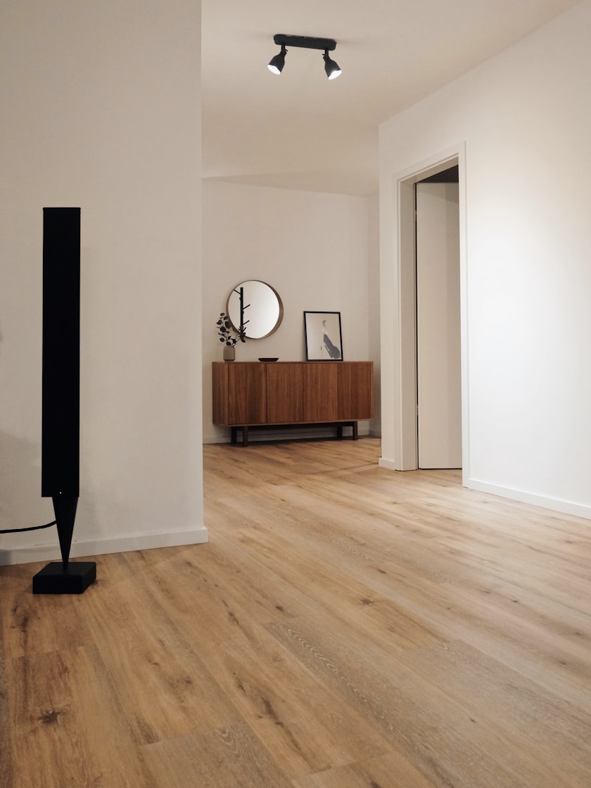 A pale hallway with an oak floor, a walnut sideboard and a round wall mirror.