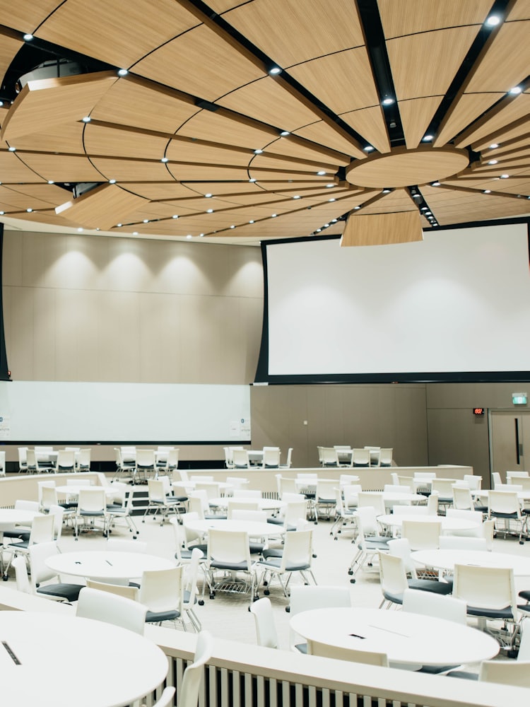 A large exhibition hall laid out with round tables and a projection screen.