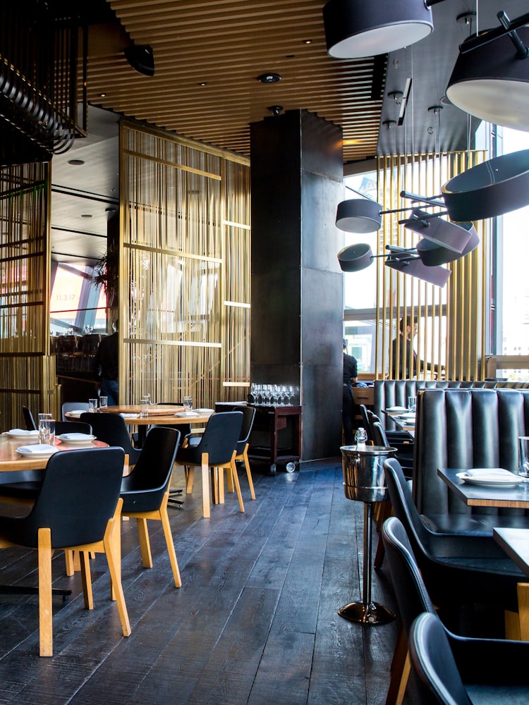 A restaurant interior with timber panelling, dark banquettes and pendant lighting.